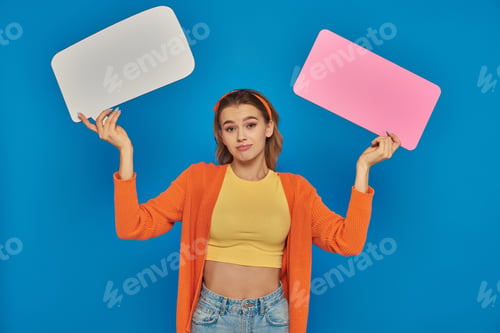 Preview: confused young woman in casual attire holding speech bubbles on blue background, space for text