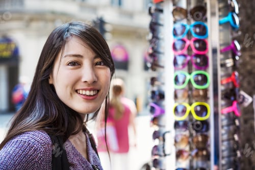 Preview: A young Japanese woman smiling at the camera, by a sunglasses display.