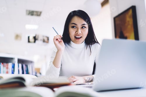 Preview: Asian adult student in formal clothes with pen in raised hand rejoicing solution while