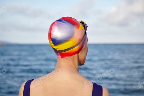 Preview: Mature woman wearing swimming costume and swimming hat, standing beside the sea, rear view