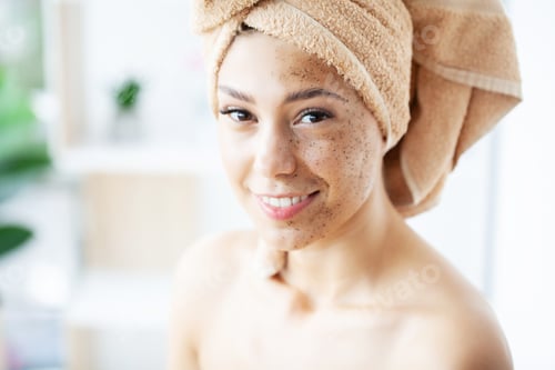Preview: Young happy woman in towel making facial massage with organic face scrub in stylish bathroom.
