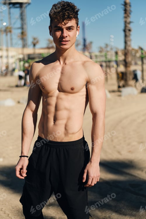 Preview: Young handsome man with naked torso confidently looking in camera after workout outdoor