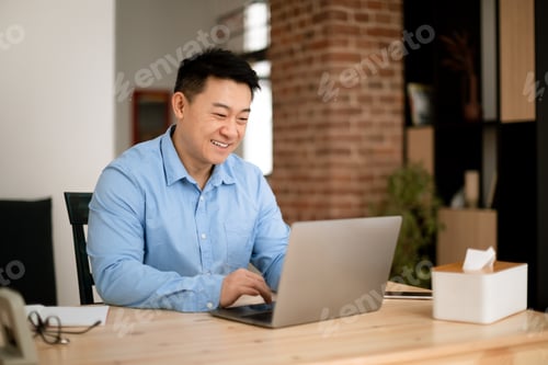 Preview: Positive asian middle aged male entrepreneur working on laptop at home office, sitting at workplace
