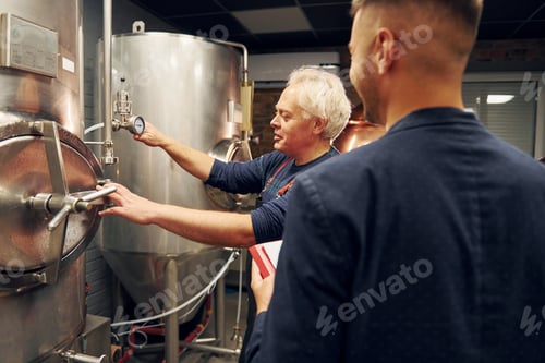 Preview: Senior man and young worker with document is standing in the storage beer room