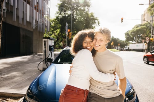 Preview: Couple embracing while charging their electric vehicle on a sunny day