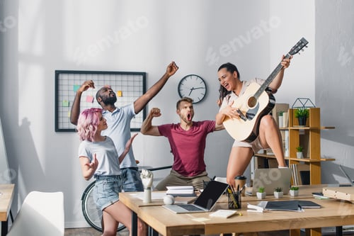 Preview: Selective focus of businesswoman playing acoustic guitar near multicultural colleagues singing and