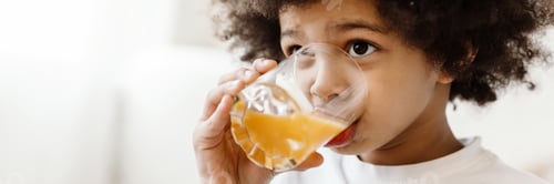 Preview: Black curly boy looking forward while drinking juice indoors