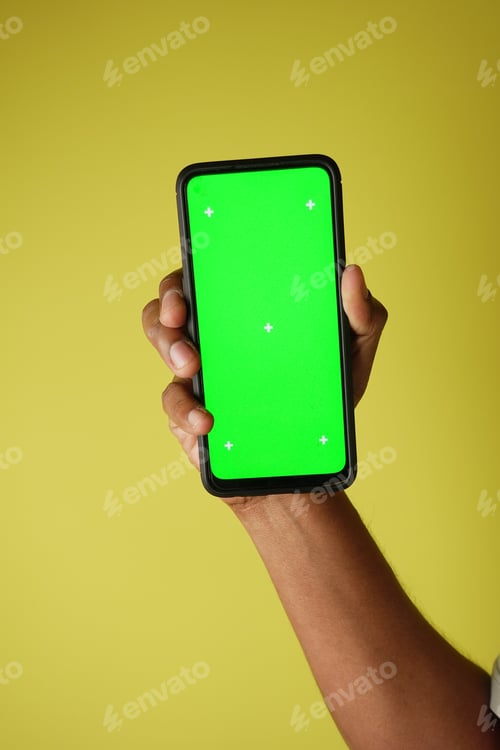 Preview: Hand holding smartphone with green screen on yellow background