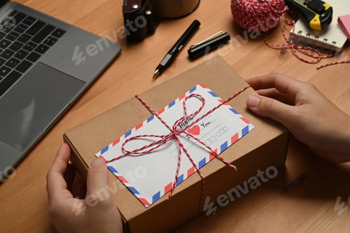 Preview: Hands holding gift box with greeting card, preparing present for family during holiday season.