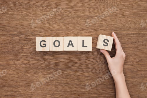 Preview: cropped view of person adjusting 'goals' word made of wooden blocks on wooden tabletop, goal setting