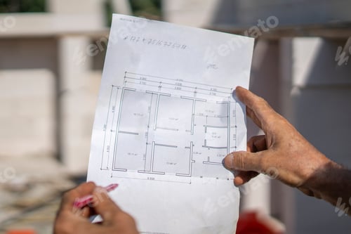 Preview: A construction worker holds a detailed plan while overseeing a house construction site.