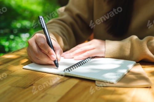 Preview: Closeup image of a young woman writing on a notebook in the outdoors
