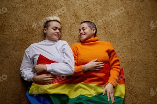 Preview: Happy relaxed lesbian woman lying on floor covering with colorful rainbow flag