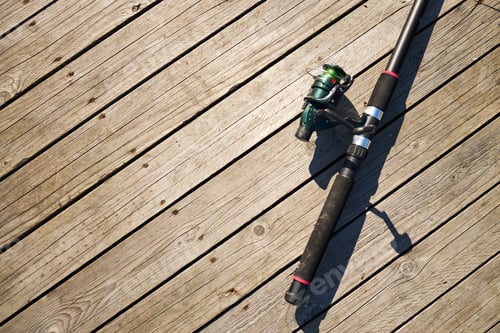 Preview: Fishing Rod Lying on Wooden Pier Decking under Bright Sunlight Outdoors