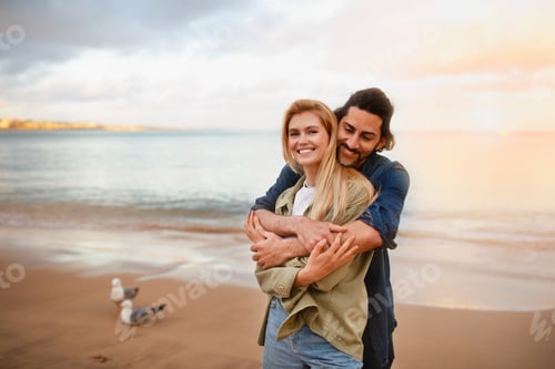 Vista previa: Romantic young man and woman embracing on the beach at sunset time