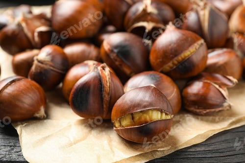 Preview: Tasty roasted edible chestnuts on black wooden table, closeup