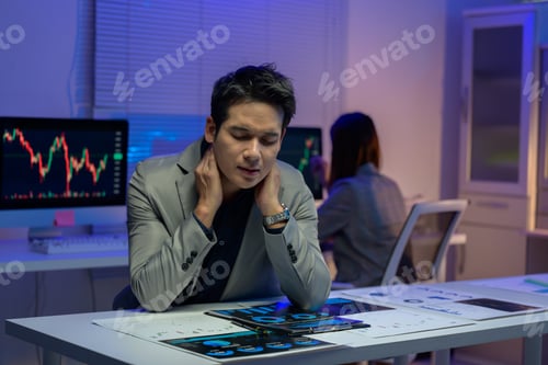 Preview: Tired businessman suffering from neck pain while working late at night in office