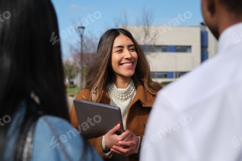 Preview: University student smiling and holding tablet talking with colleagues outdoor