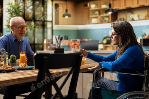 Preview: Aged woman with chronic impairment serves coffee at breakfast with husband