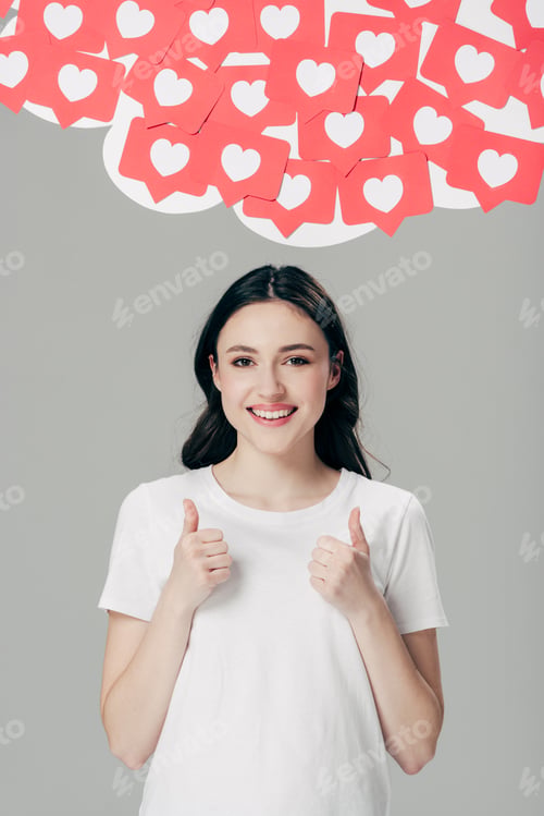 Preview: cheerful pretty girl in white t-shirt showing thumbs up near red paper cut cards with hearts symbols