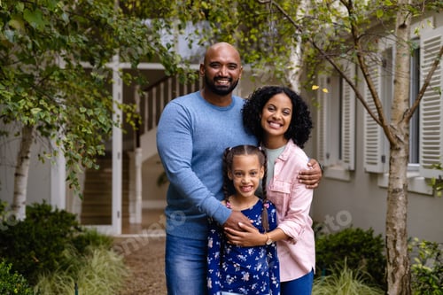 Preview: Portrait of happy biracial parents and daughter embracing in garden outside house