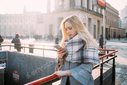 Preview: Young woman looking at smartphone by underground station, Milan, Italy
