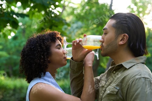 Preview: Young couple sharing orange juice in a park