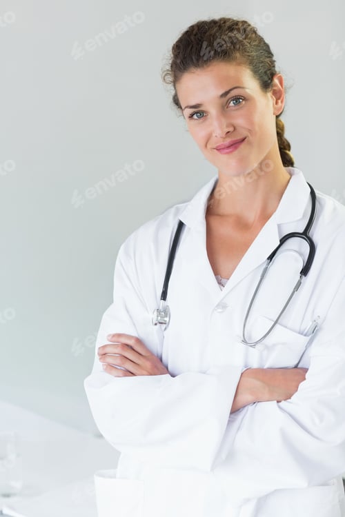 Preview: Female doctor crossing arms in clinic with white coat, stethoscope, glass on table left, copy space
