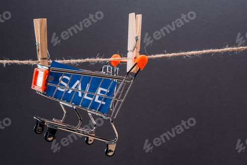 Preview: Close-up view of small shopping cart with sale sign hanging on rope isolated on grey, big sale