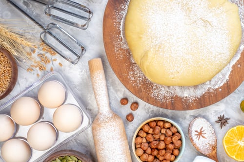 Preview: Overhead view of raw pastry flour on round board hazelnuts eggs lemon on stained white background