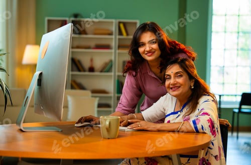 Preview: Indian mother and daughter enjoy using computer together at home while shopping pointing happily