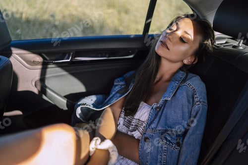 Preview: Horizontal shot of a beautiful young caucasian female posing in the back seat of a car in a field