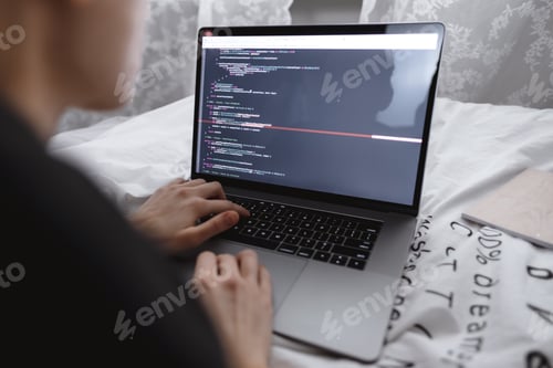 Preview: Young female programmer writes program code on a computer laptop in the bed at home. remote work