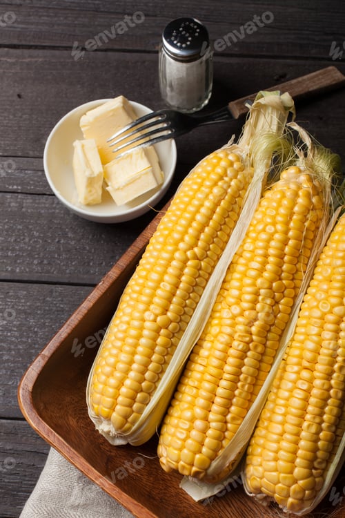 Preview: Fresh corn on the cob with salt and butter on wooden table, closeup, top view. Dark background