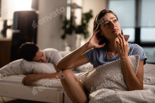 Preview: Pensive woman with mobile phone thinking of something while her boyfriend is sleeping.