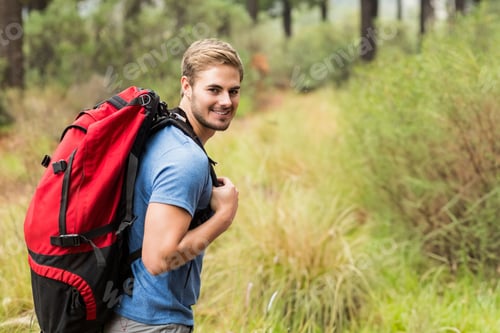 Preview: Male hiker hiking on pine forest trail smiling, carrying red backpack with black straps, copy space