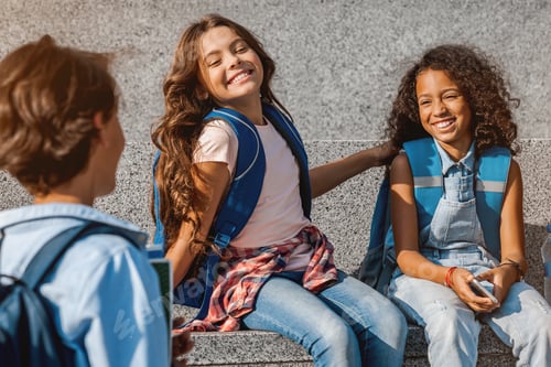 Preview: Group of school childrens sitting on the steps and having fun outdoors