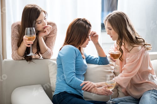 Preview: Two young women comforting their friend while holding glasses with wine