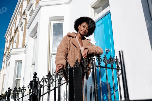 Preview: Fashion black woman posing beside a blue door outdoors.