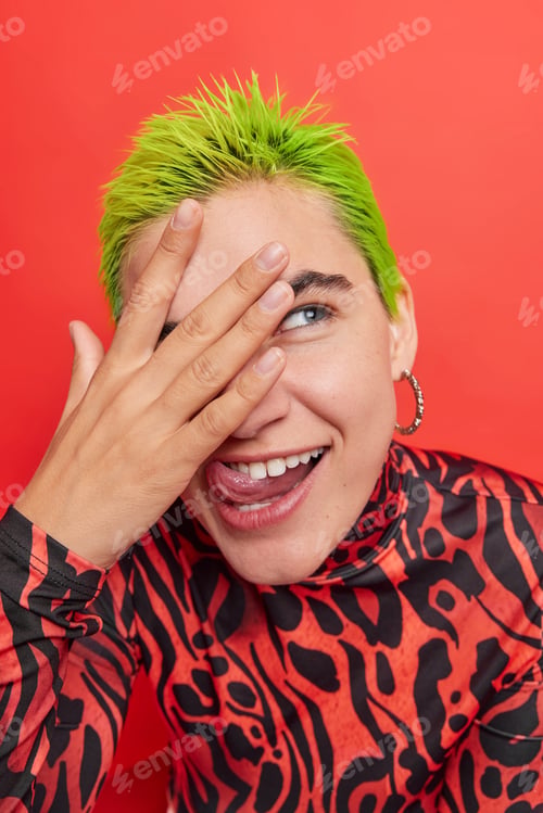 Preview: Vertical shot of funny extraordinary hipster girl with green hair sticks out tongue looks through fi