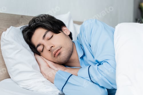 Preview: young brunette man in blue pajamas sleeping on white bedding