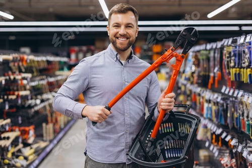 Preview: Smiling man finding a metal cutter in a tool shop, preparing for renovation work