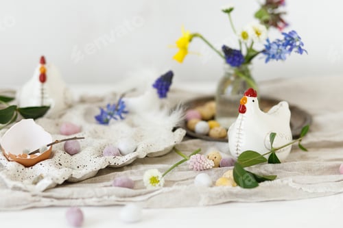 Preview: Colorful easter chocolate eggs in nest, spring flowers, chicken figurine and linen cloth