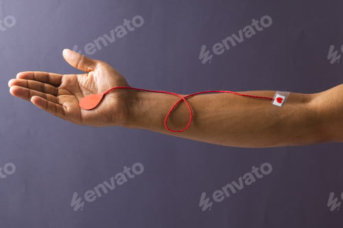 Preview: Arm of biracial man with heart sticking plaster and red string with blood drop, on grey background