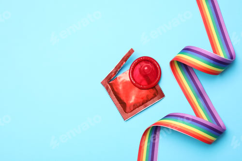 Preview: Red condom and rainbow ribbon on light blue background, flat lay. LGBT concept