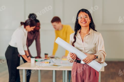 Preview: Asian woman architect posing in the office during a meeting and holding blueprints
