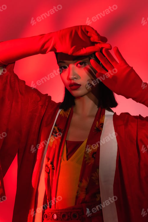 Preview: young asian woman in elegant kimono cape and gloves posing on abstract background with red shade