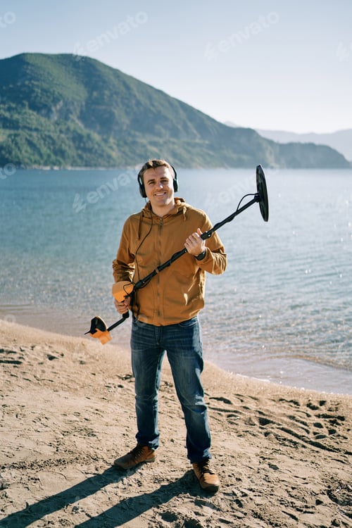 Preview: Smiling beach cop with a metal detector stands on the seashore