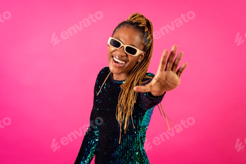 Preview: A black ethnic woman with braids dancing at party on a pink background, smiling looking at camera