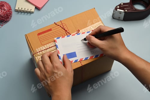 Preview: Above view of man signing greeting card, surrounded by gift wrapping materials on blue background.